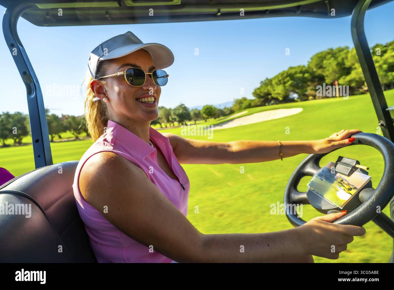 Golfista sorridente che guida un golf cart attraverso uno splendido campo da golf soleggiato, godendosi il vivace paesaggio verde e le attività all'aperto Foto Stock