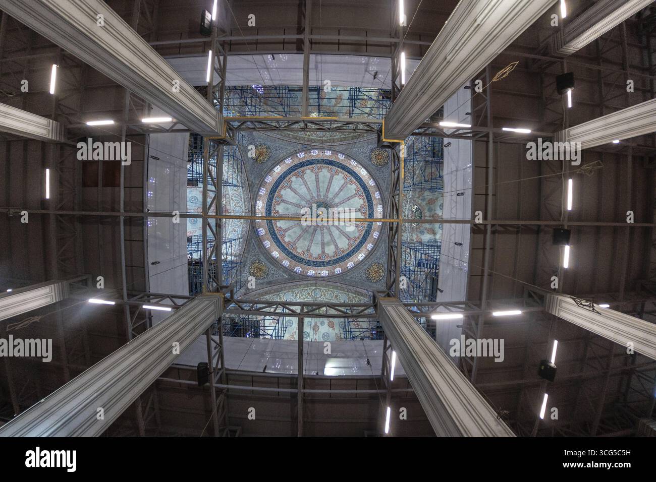 Vista grandangolare che cattura i lavori di restauro in corso all'interno di una moschea, mettendo in evidenza impalcature che racchiudono una cupola splendidamente decorata, che mostra intr Foto Stock