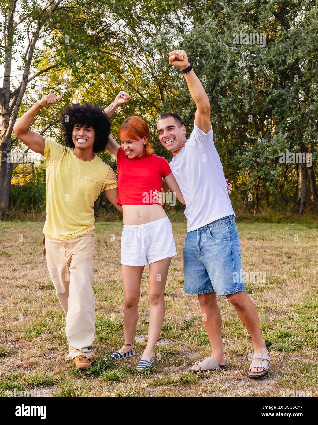 Tre amici felici che festeggiano con le braccia alzate in un parco Foto Stock