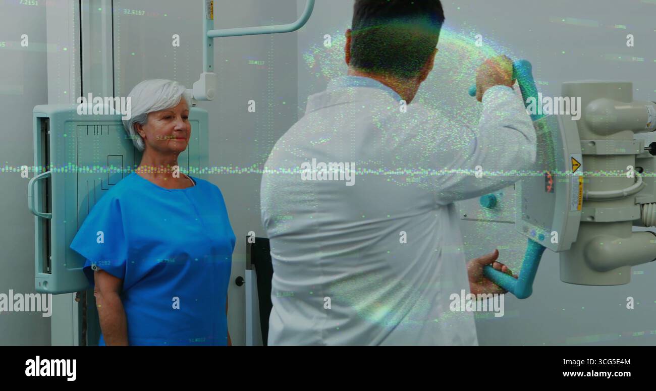 Paziente in posizione eretta in un camice in ospedale con pannello rilevatore, tecnico che regola le maniglie radiologiche dell'arco C. Foto Stock