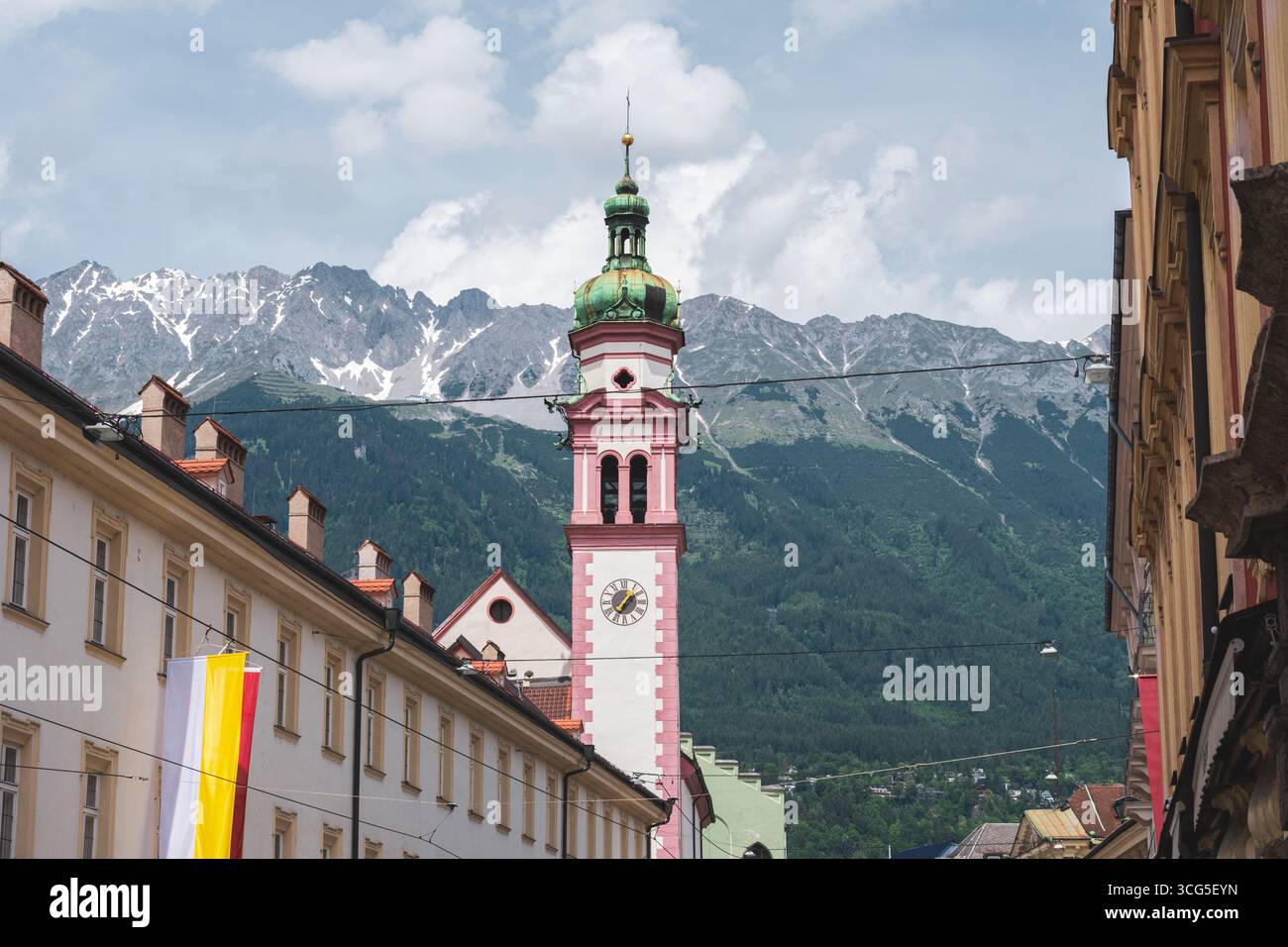 Una storica torre dell'orologio barocco a Innsbruck, Austria, che sorge sopra gli edifici della città vecchia con le Alpi Nordkette sullo sfondo. Foto Stock