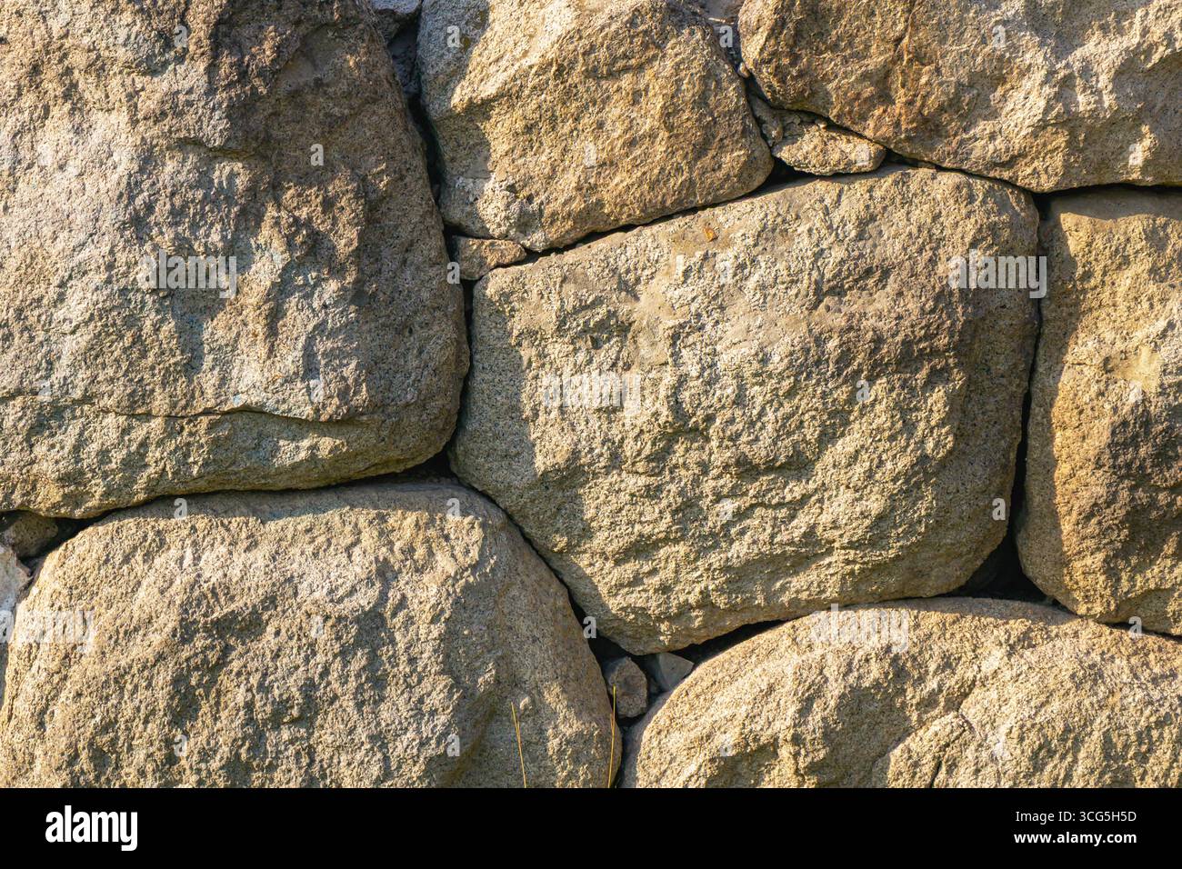 Una robusta parete costruita con grandi pietre intemprate mostra un'estetica rustica in un ambiente di campagna. La luce del sole proietta toni caldi sull'tex Foto Stock