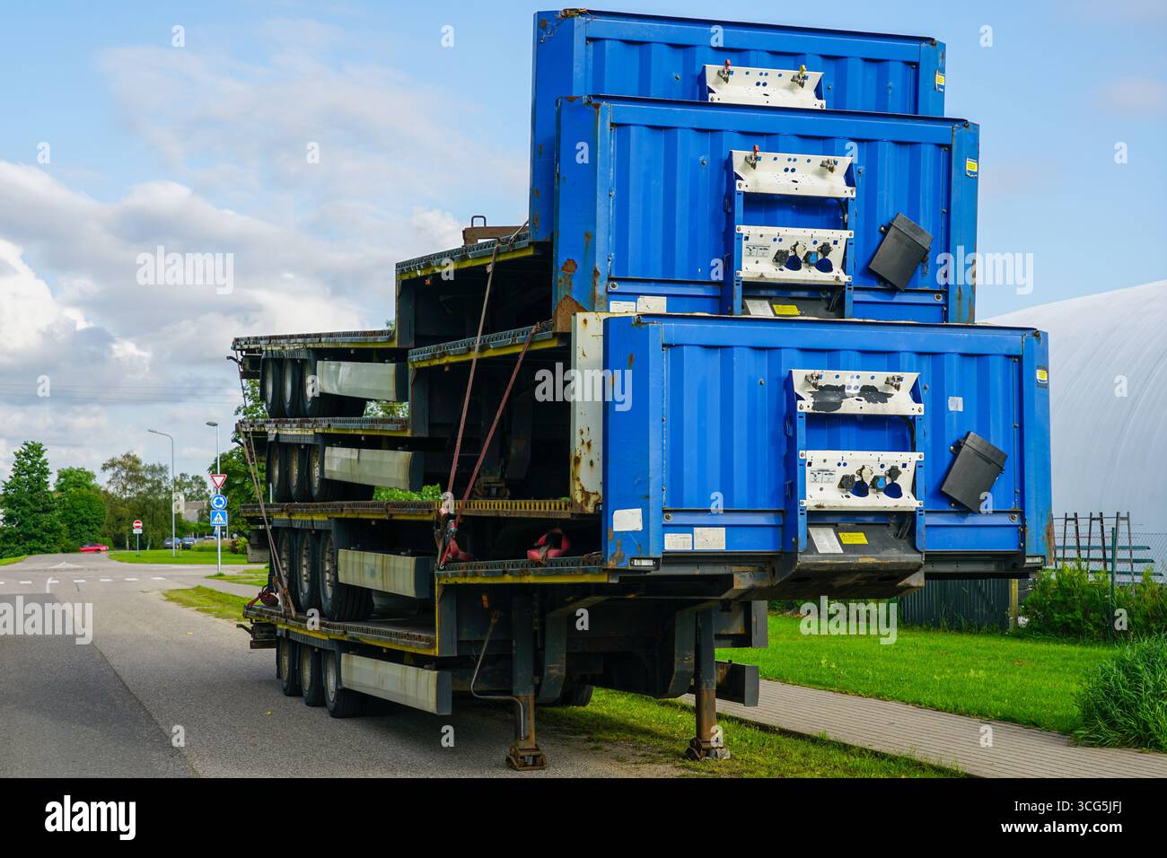 Quattro telai per rimorchi blu impilati per la logistica dei trasporti, parcheggiati sul ciglio della strada sotto il cielo nuvoloso Foto Stock