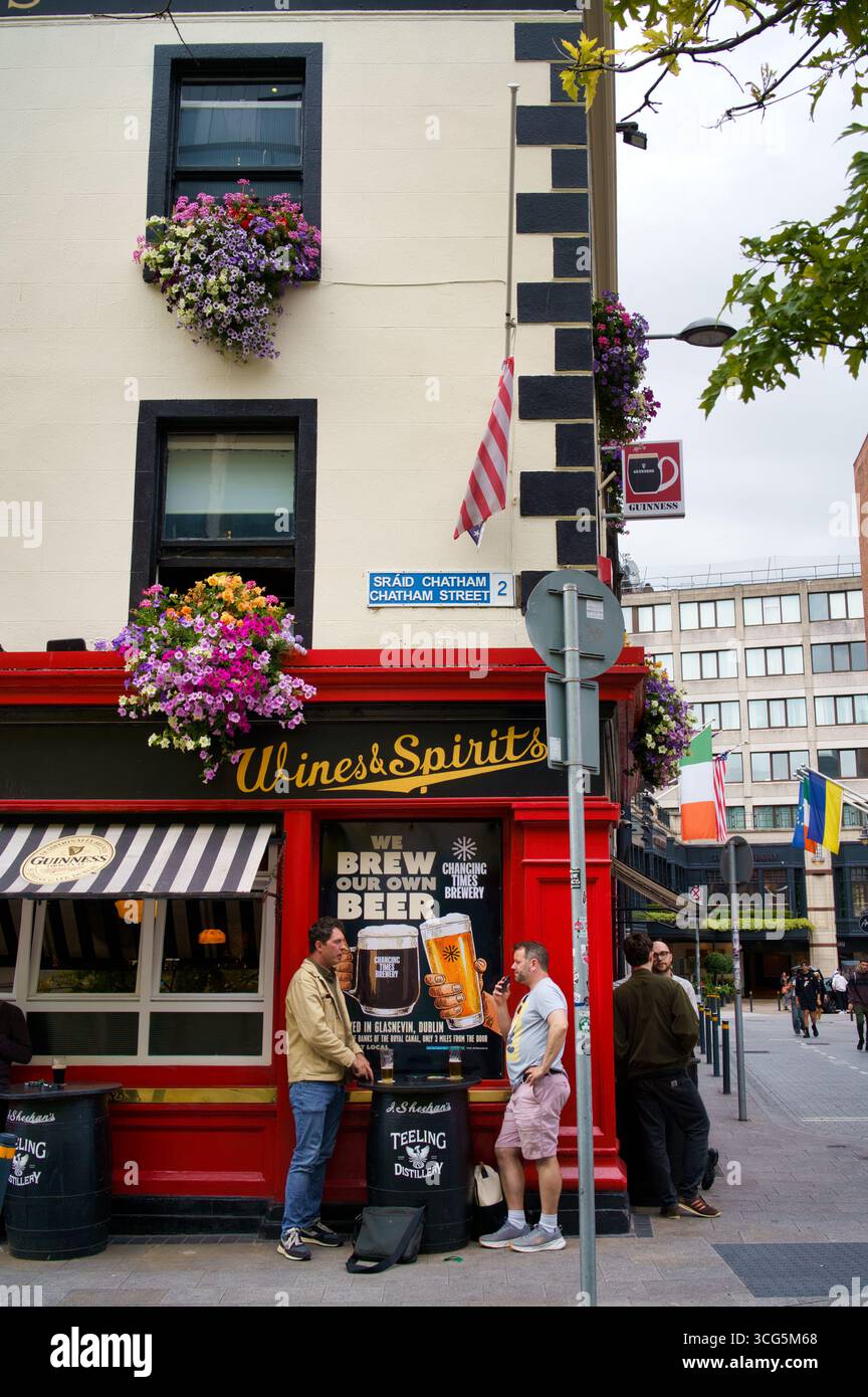 Una vivace scena di strada a Dublino, Irlanda, che mostra un pub tradizionale con fiori colorati e gente che si gode l'atmosfera. Foto Stock