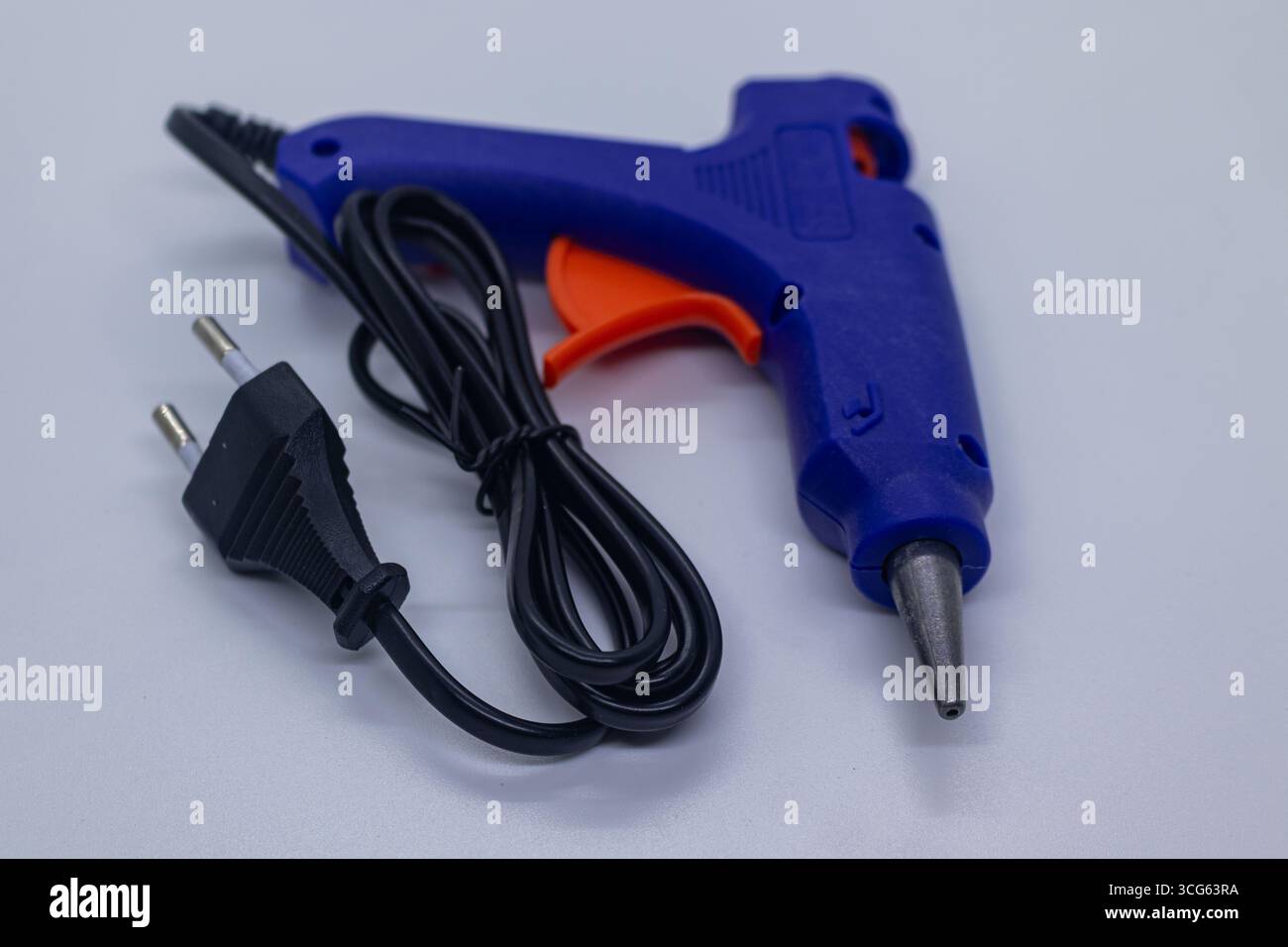 Pistola per colla calda elettrica blu con cavo di alimentazione nero su sfondo bianco Studio. Foto Stock