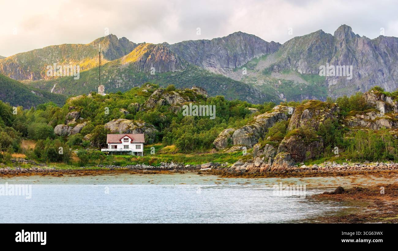 Paesaggio costiero panoramico caratterizzato da un'affascinante casa annidata tra colline rocciose e vegetazione lussureggiante, con maestose montagne che si innalzano sullo sfondo, cap Foto Stock