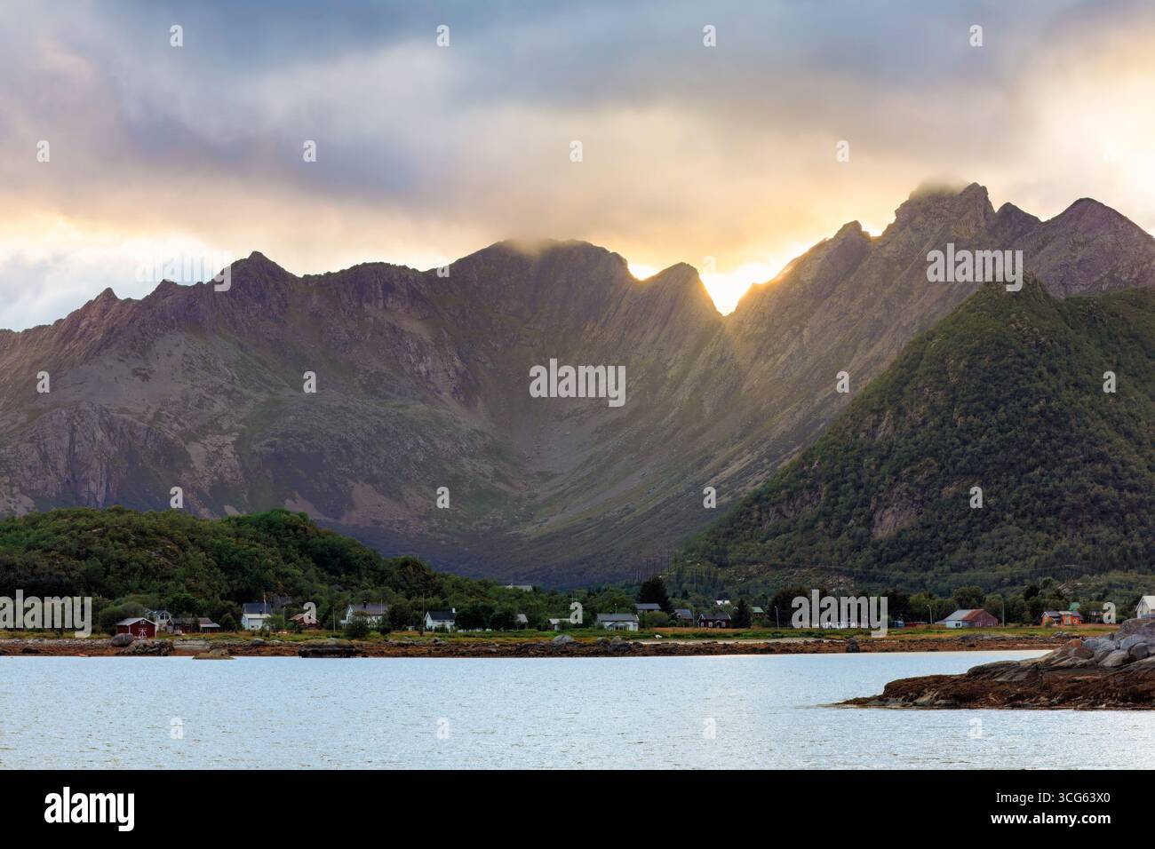 La suggestiva catena montuosa si erge su acque calme, con la luce del sole che attraversa le nuvole, emettendo un caldo bagliore sul terreno accidentato e migliorando il se stesso Foto Stock
