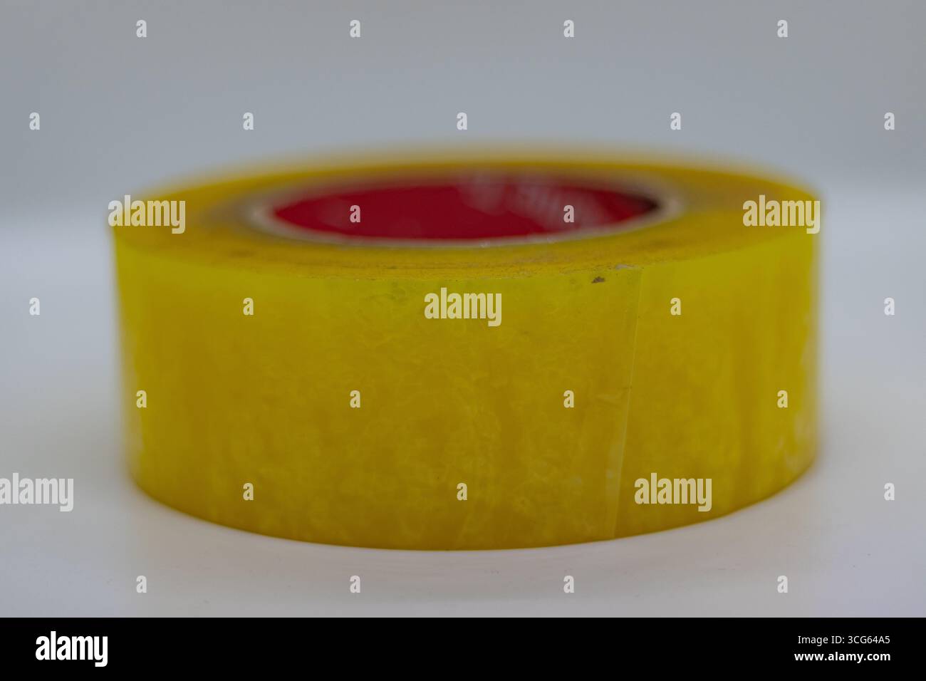 Primo piano di un rotolo di nastro adesivo giallo brillante utilizzato per la spedizione e lo stoccaggio. Nastro da imballaggio resistente su sfondo bianco pulito, ideale per l'imballaggio. Foto Stock