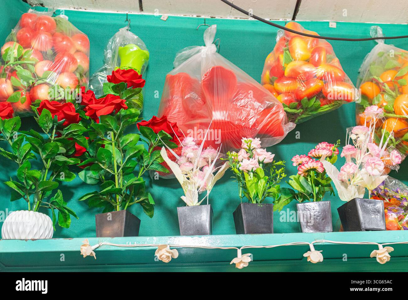 Fiori e frutti artificiali luminosi e colorati disposti su un vivace sfondo verde. Perfetto per espositori decorativi, progetti artigianali, arredamento per la casa, Foto Stock