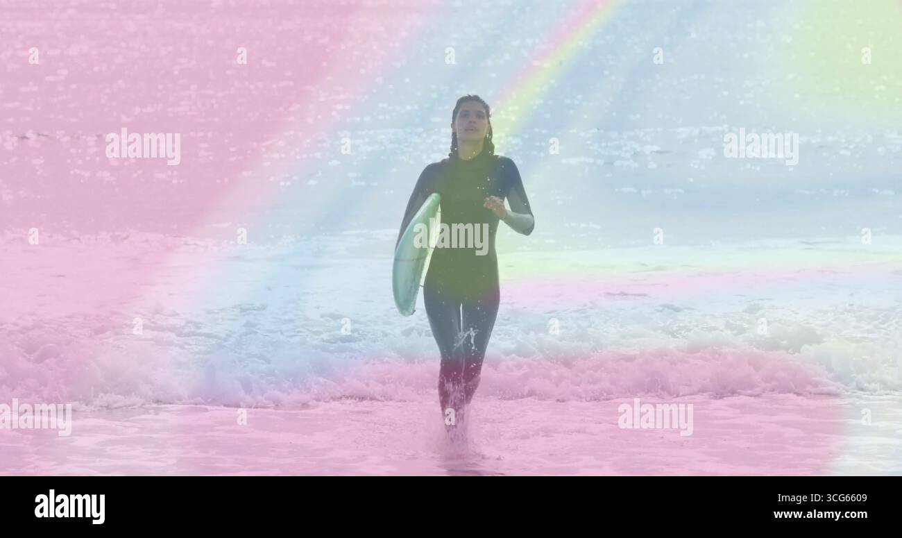 Surfista emergente in muta che strizza tra le onde in spiaggia, trasportando tavole da surf turchesi e pastelli Foto Stock