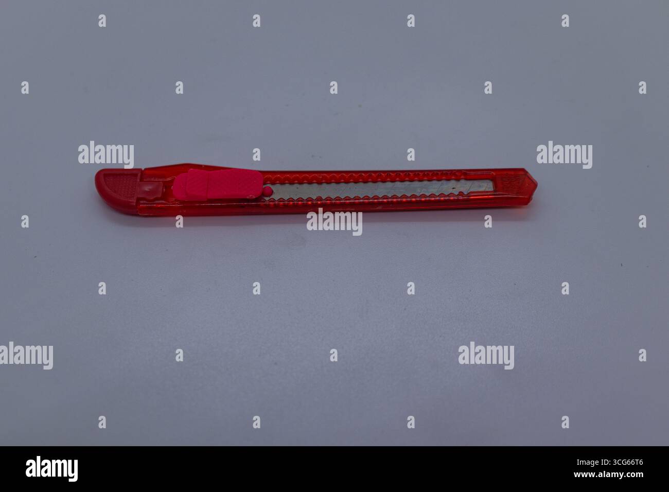 Coltello da cartoleria rosso compatto con lama retrattile, ideale per il taglio di carta, cartone e imballaggio. Strumento di utilità per ufficio e scuola su bianco Foto Stock