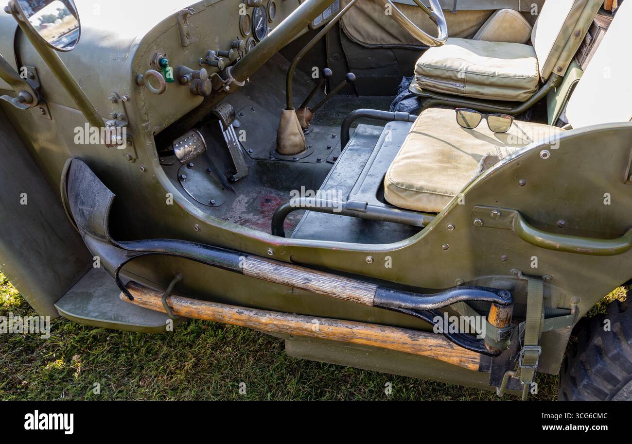 Vista interna di una vecchia jeep militare che mostra il sedile del conducente e il cruscotto con attrezzi rustici fissati lateralmente Foto Stock