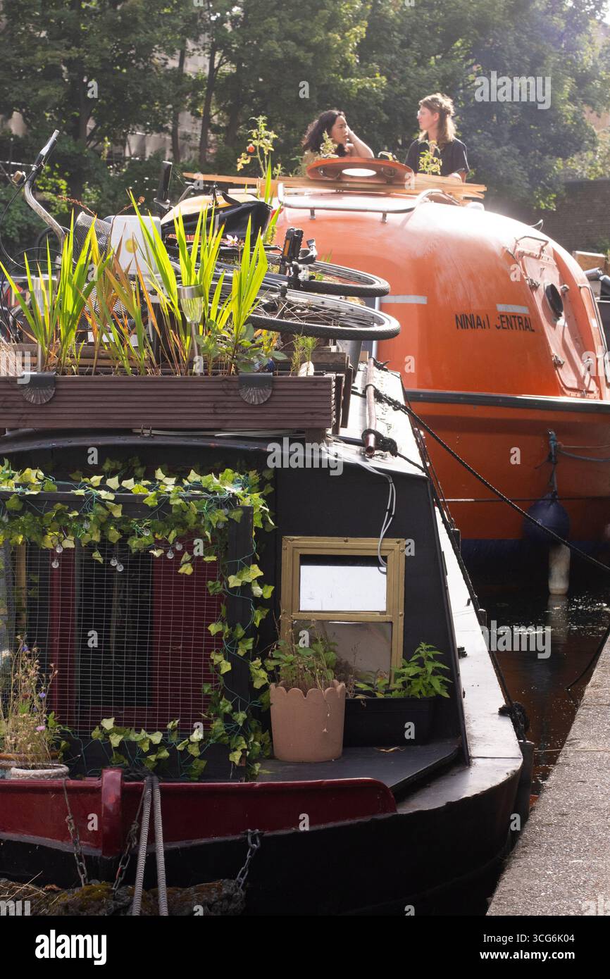 Due persone chiacchierano in cima al motoscafo Ninia Central, ormeggiato lungo il Regent's Canal a Londra. Le case galleggianti sono una visione comune e offrono una vita alternativa Foto Stock