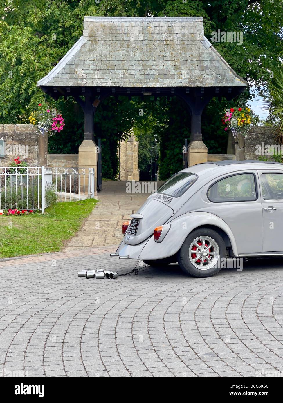 Un Maggiolino Volkswagen bianco d'epoca aggiunge fascino alla scena di un matrimonio a Sedgefield, Regno Unito, ambientato contro una chiesa storica e un raduno formale Foto Stock
