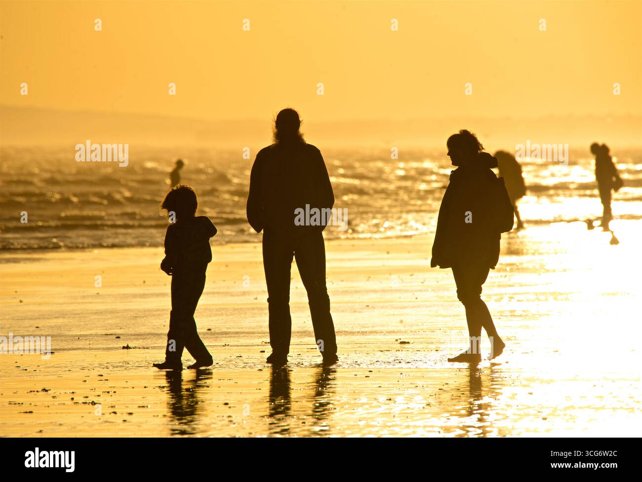 Gente che si gode la bassa marea al tramonto. Sagome di persone e Shoreham Power Station in lontananza. Brighton e Hove, Inghilterra, Regno Unito Foto Stock