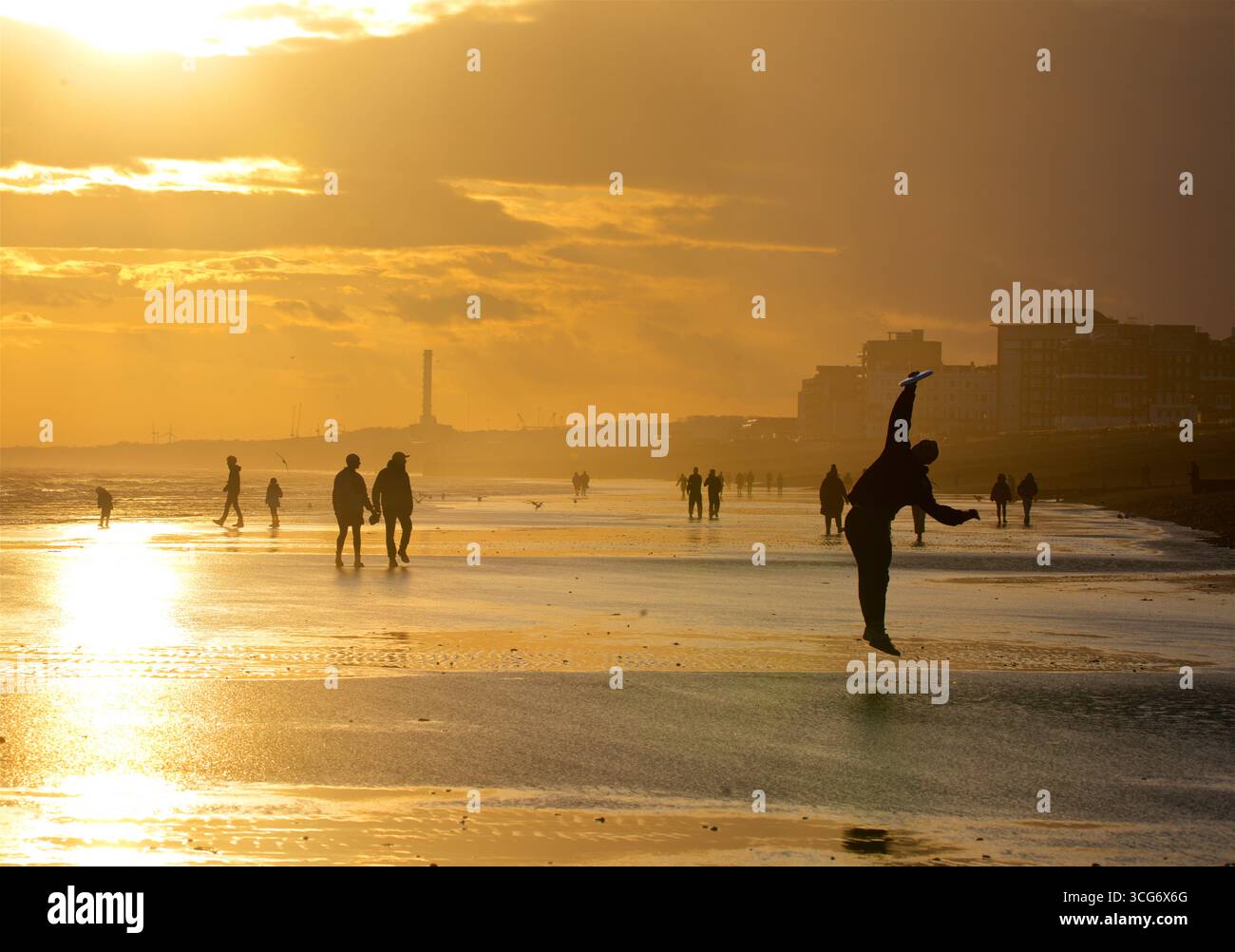 Sagome di persone che amano la spiaggia e giocano a frisbee con la bassa marea, Brighton e Hove, Inghilterra, Regno Unito Foto Stock