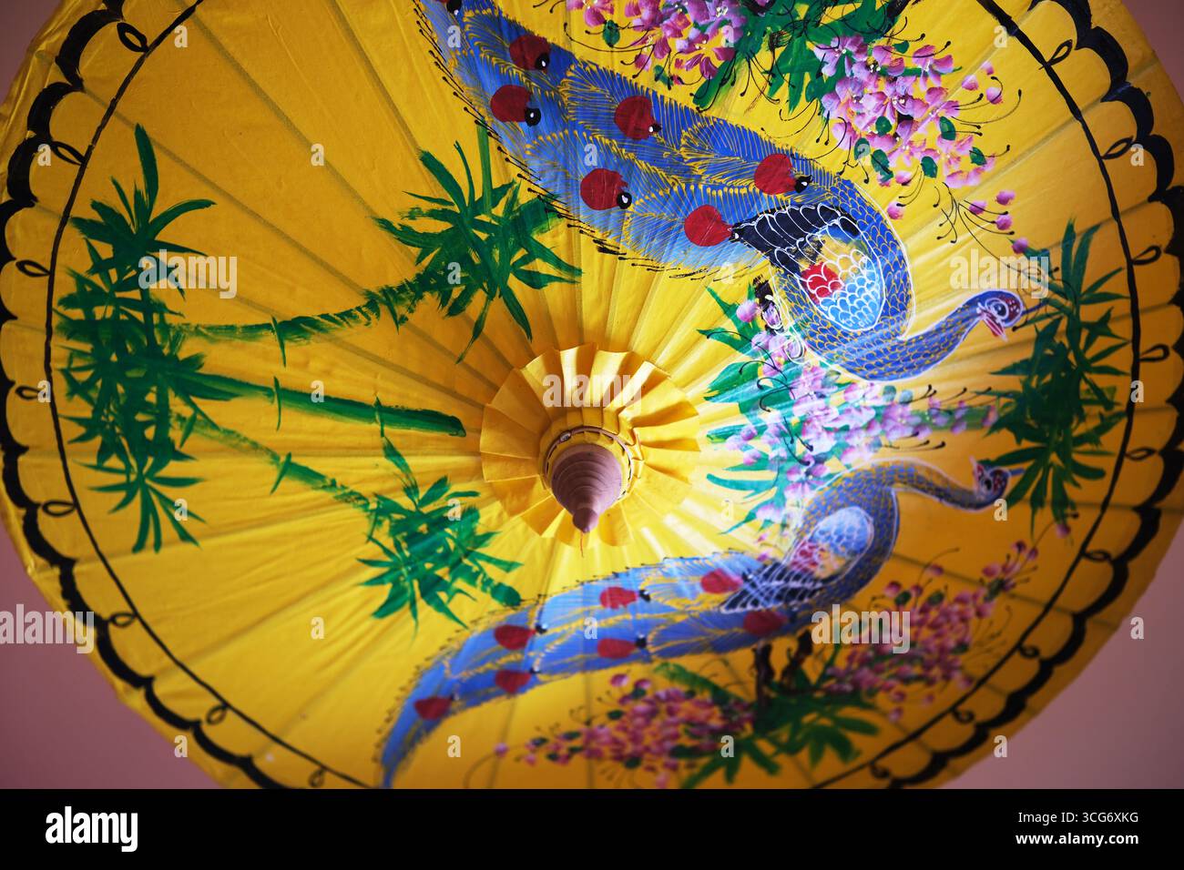 Sanya,Hainan,Cina-20 aprile 2025: Ombrello di carta giallo asiatico con pavone e motivi floreali Foto Stock