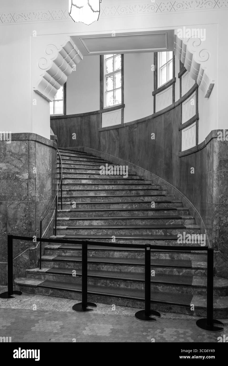 Immagine monocromatica che mostra una scala ricurva splendidamente progettata in un edificio storico caratterizzato da marmo e intricati dettagli architettonici Foto Stock