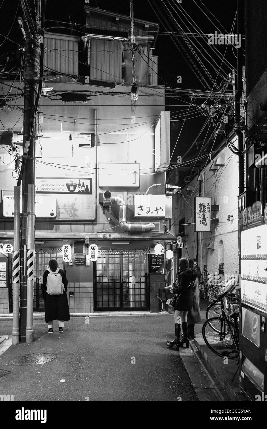 Una fotografia in bianco e nero che mostra una strada tranquilla di Kyoto, caratterizzata da strutture tradizionali, cartelli sospesi e illuminazione stradale che ne esalta la posizione Foto Stock