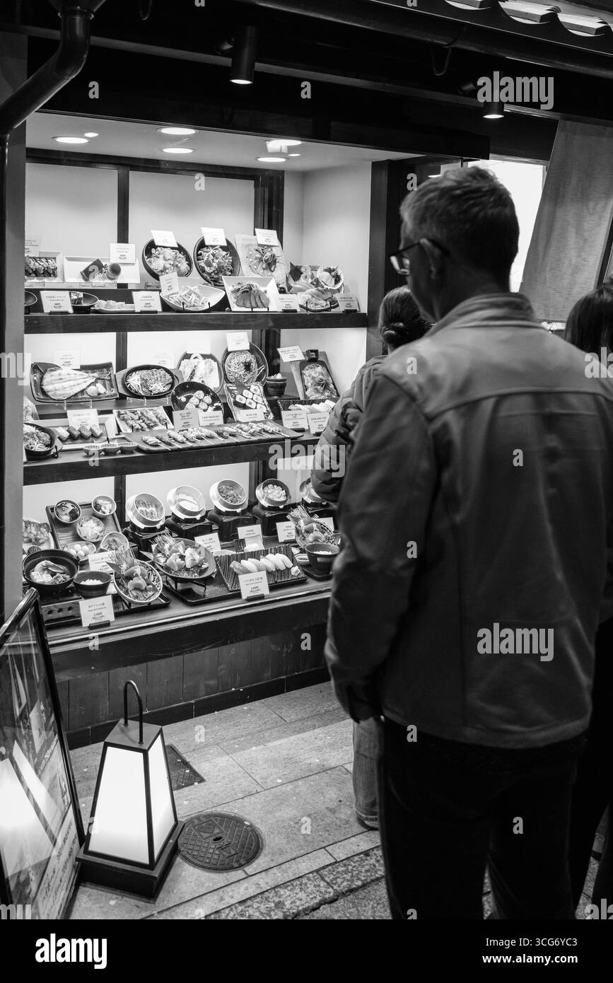 Uomo che guarda i modelli di cibo in mostra, illuminato e che mostra le opzioni per i pasti, Ponchaco, Nakagyo Ward, Kyoto, Kansai, Honshu, Giappone Foto Stock