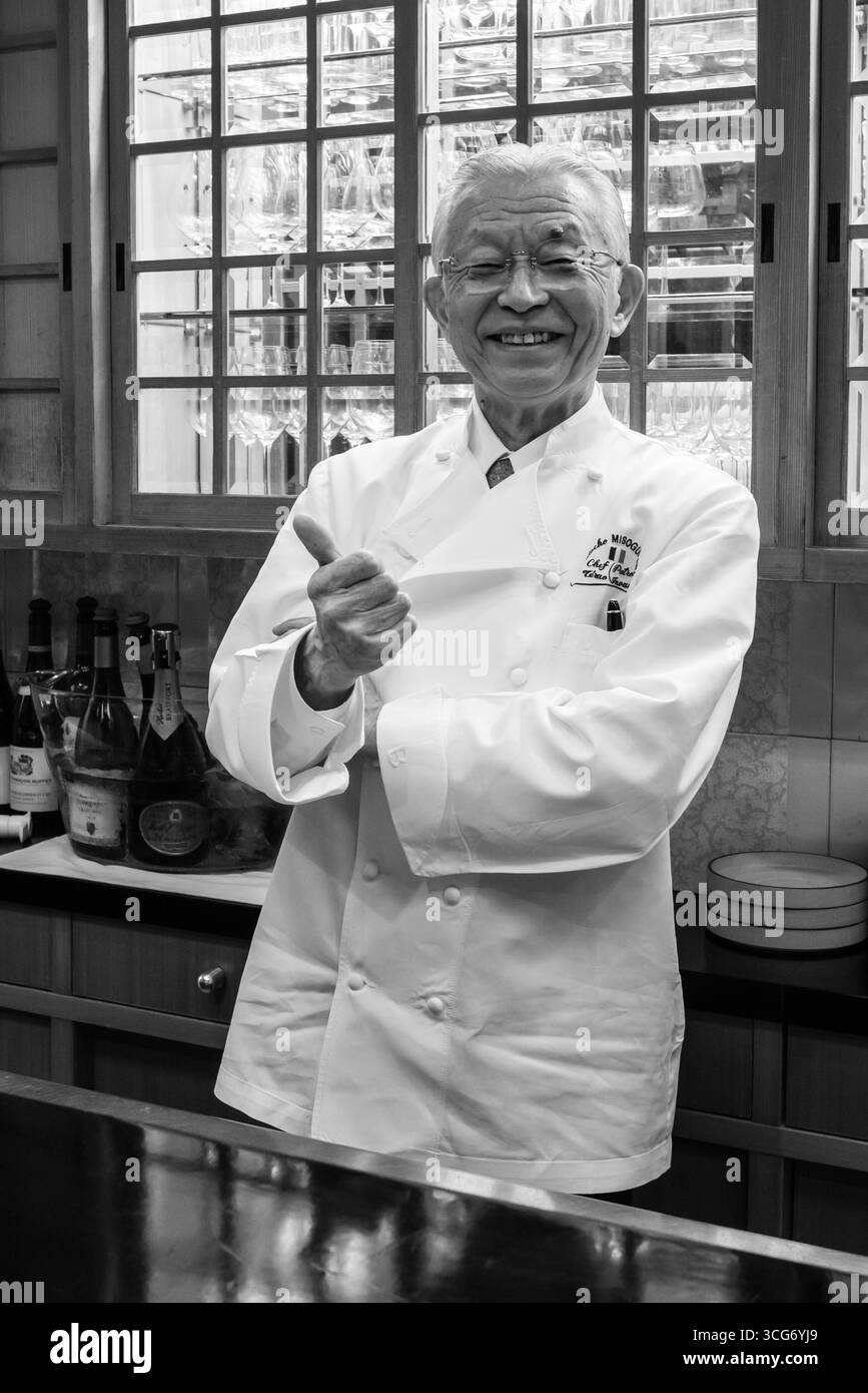 Uno chef maschile sorridente in uniforme bianca nel ristorante francese Pontocho Misoguigawa con bottiglie di vino e bicchieri sullo sfondo. Un'immagine di esperti Foto Stock