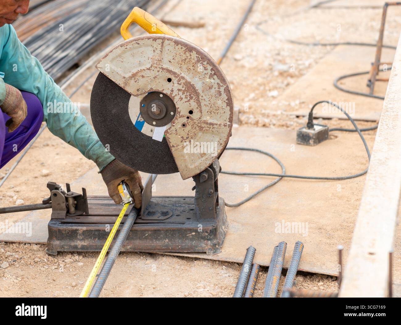 Operaio edile che misura un armatura in acciaio prima di tagliare con una sega elettrica in cantiere. Foto Stock