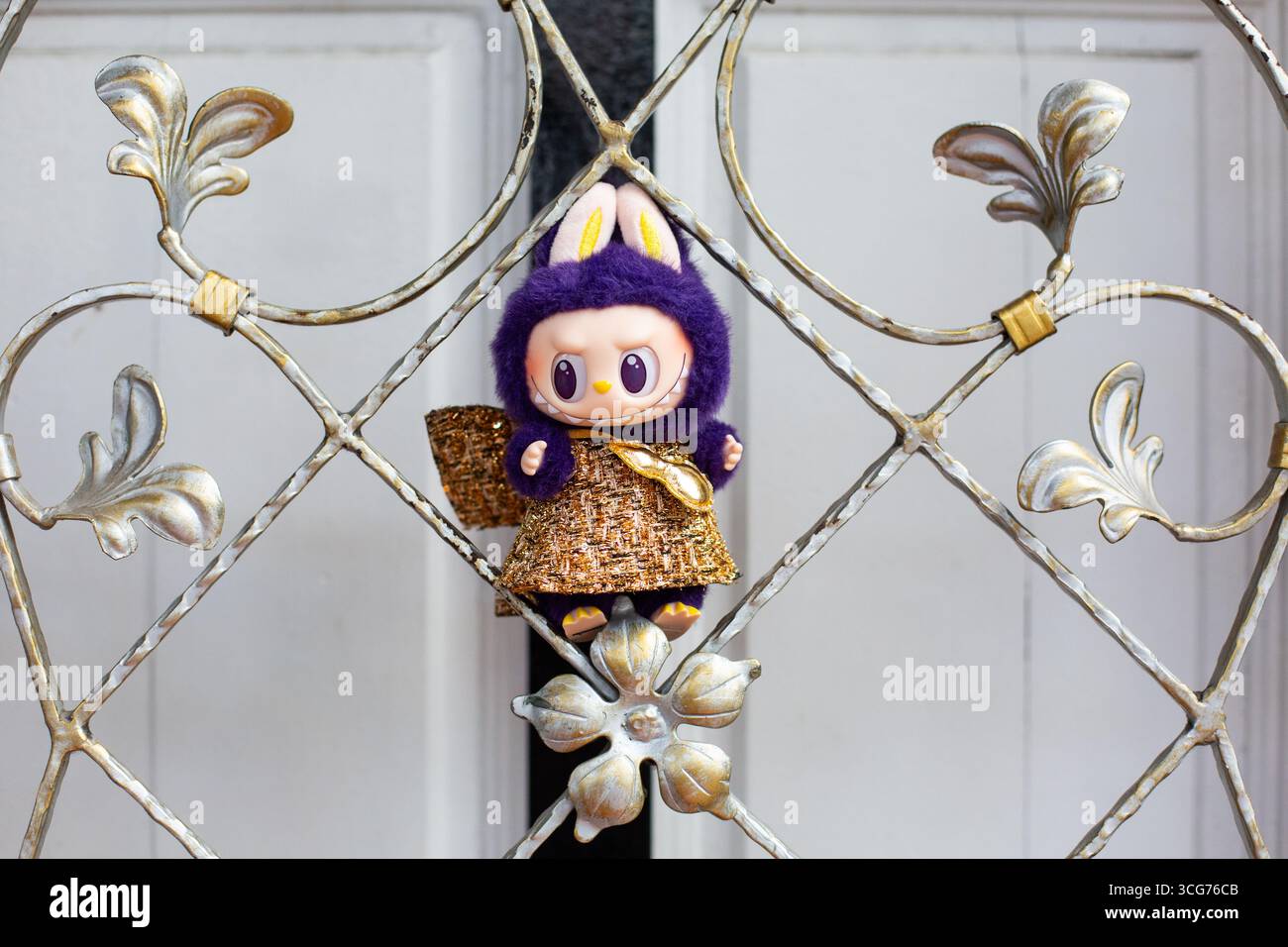 Labubu di colore viola in abito lucido dorato che poggia su un design a griglia sulla strada di Little India, composizione simmetrica. Singapore. Foto Stock