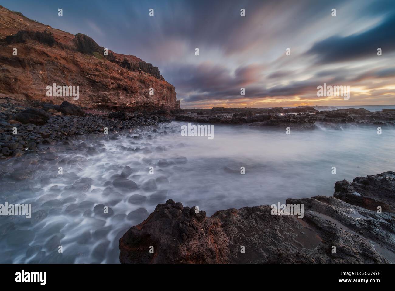 Costa rocciosa al tramonto con onde nebbiose e cielo spettacolare Foto Stock