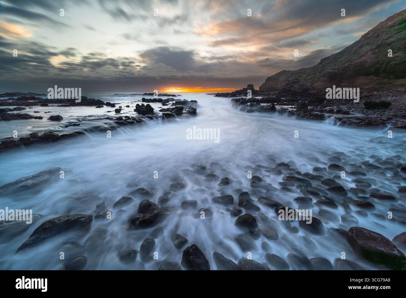 Costa rocciosa al tramonto con onde nebbiose e cielo spettacolare Foto Stock