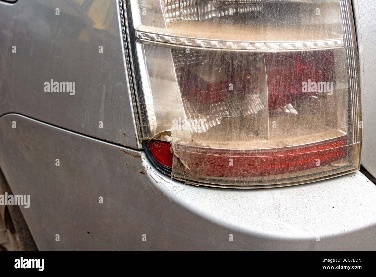 Primo piano di una luce di posizione posteriore spaccata e polverosa su un'auto color argento, che mostra danni visibili al trasparente e al pannello della carrozzeria circostante, con particolare attenzione Foto Stock