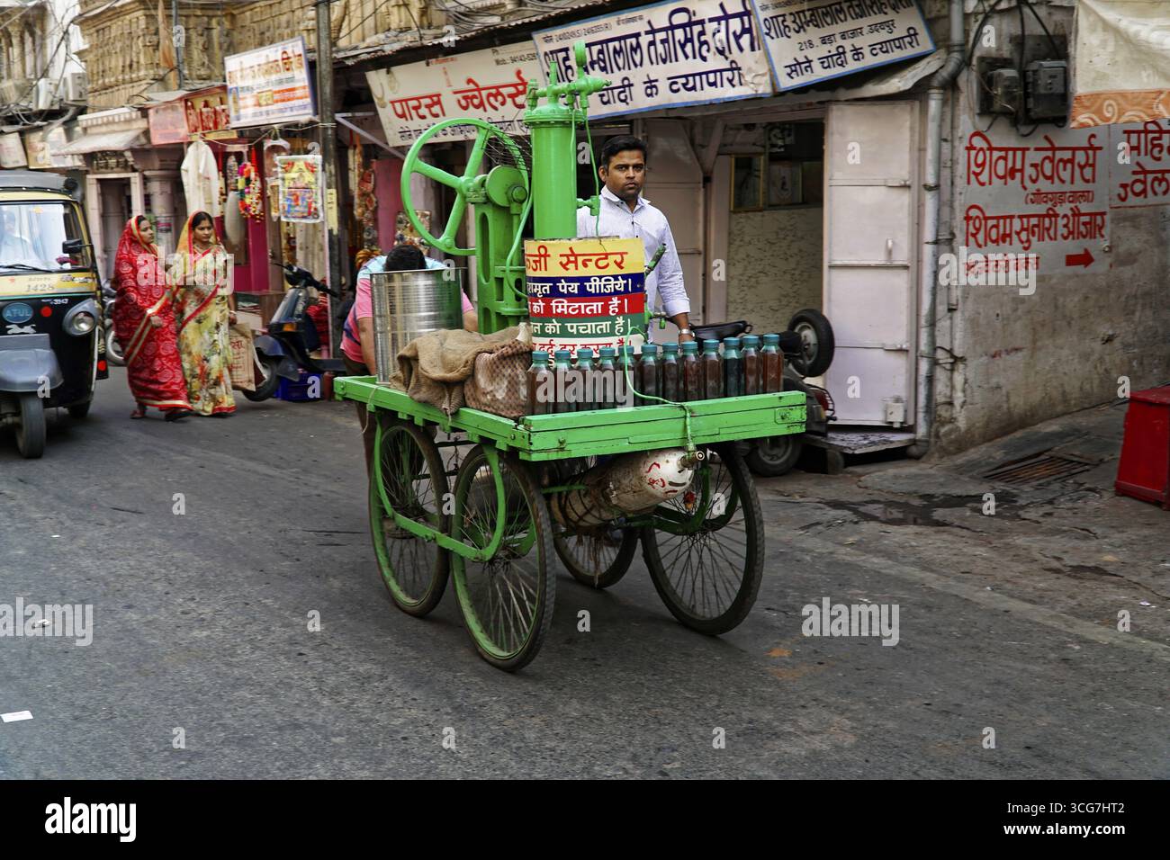 Udaipur, Rajasthan, India del Nord, Asia, uomo con tradizionale carrello per succhi di frutta all'angolo della strada trafficata Foto Stock