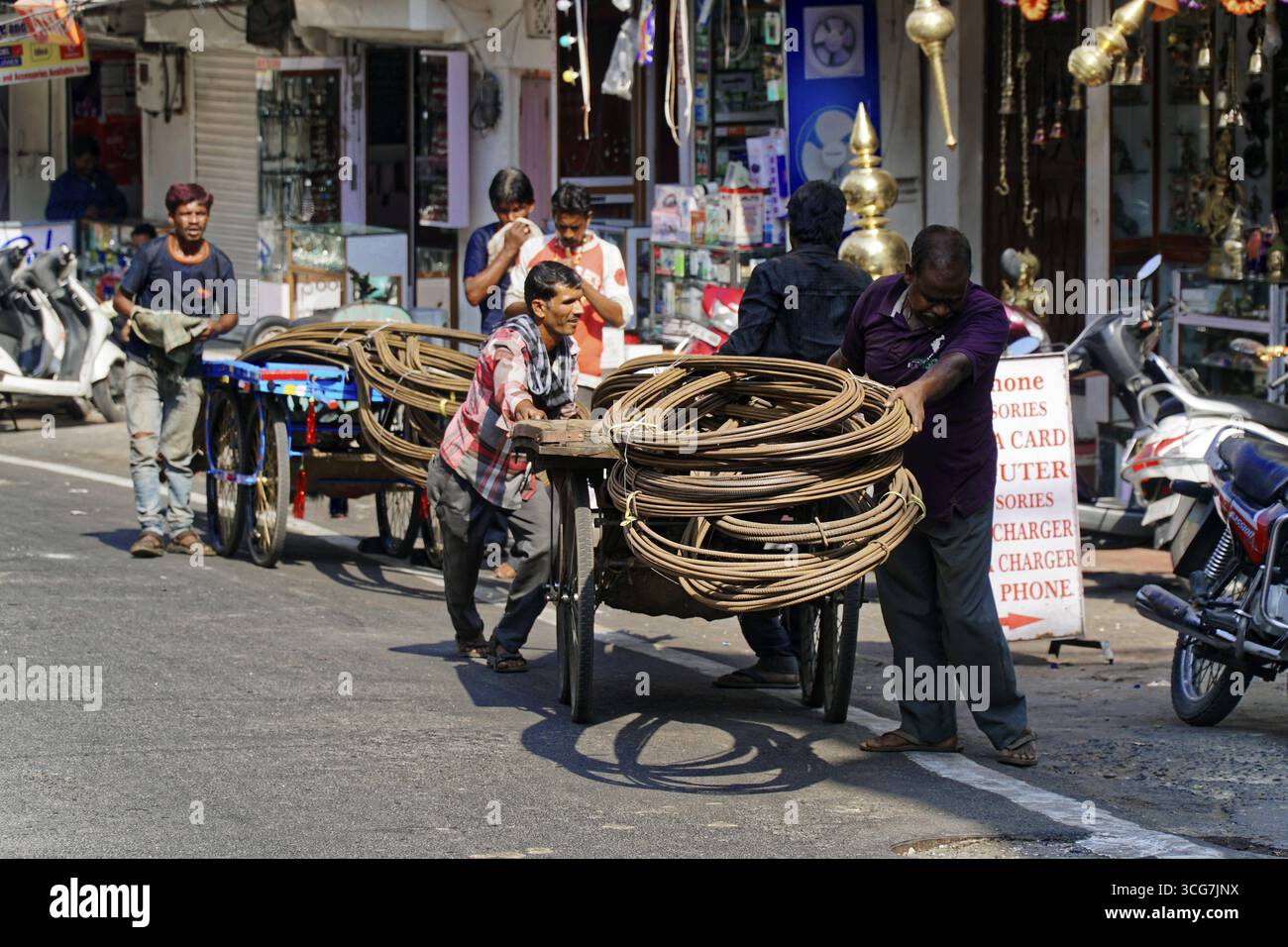 Udaipur, Rajasthan, India del Nord, Asia, diversi uomini che tirano carri di legno con corde arrotolate su una strada trafficata Foto Stock