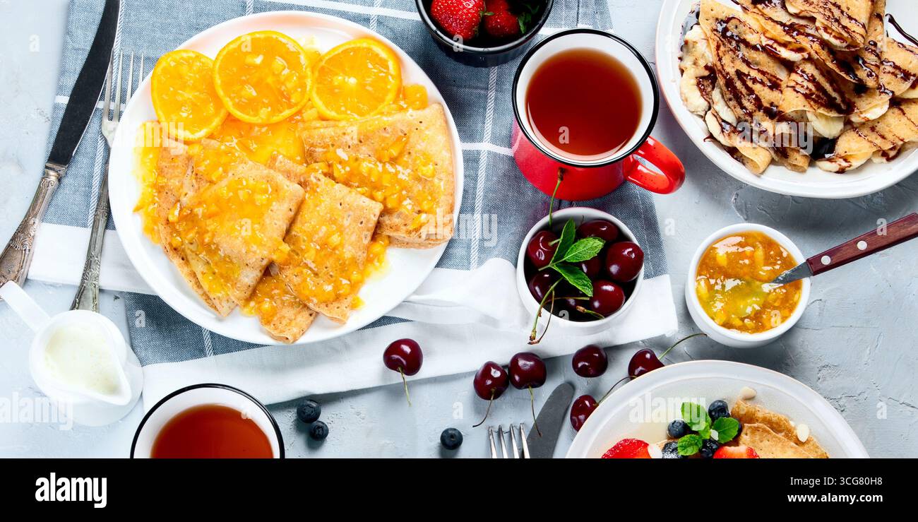 Crepe fresche con marmellata, frutta e frutti di bosco su sfondo grigio. Deliziose crepe fatte in casa. Vista dall'alto Foto Stock