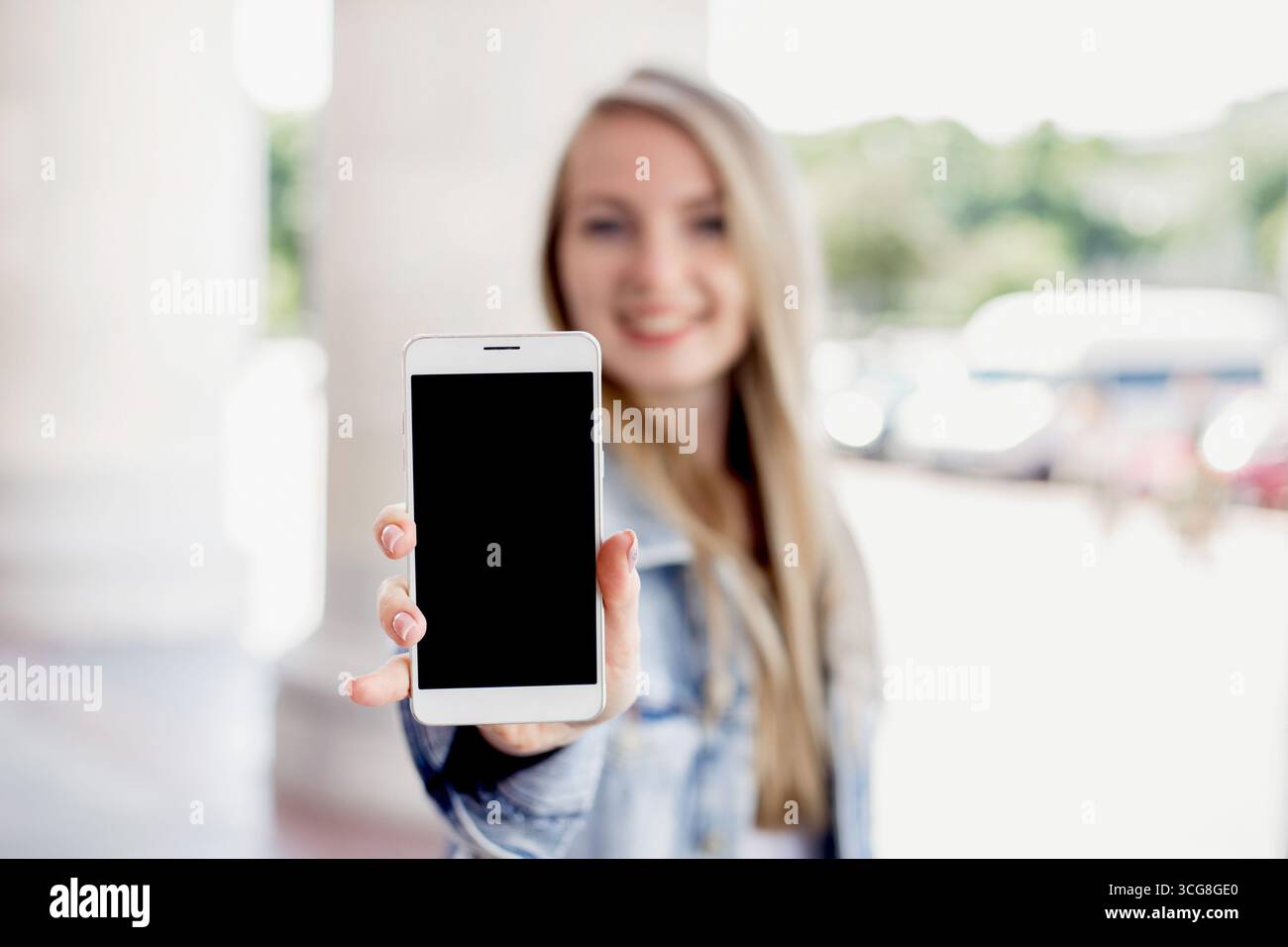 Primo piano ritratto di una studentessa sorridente che mostra uno schermo di un telefono cellulare all'aperto sullo sfondo di un edificio universitario Foto Stock