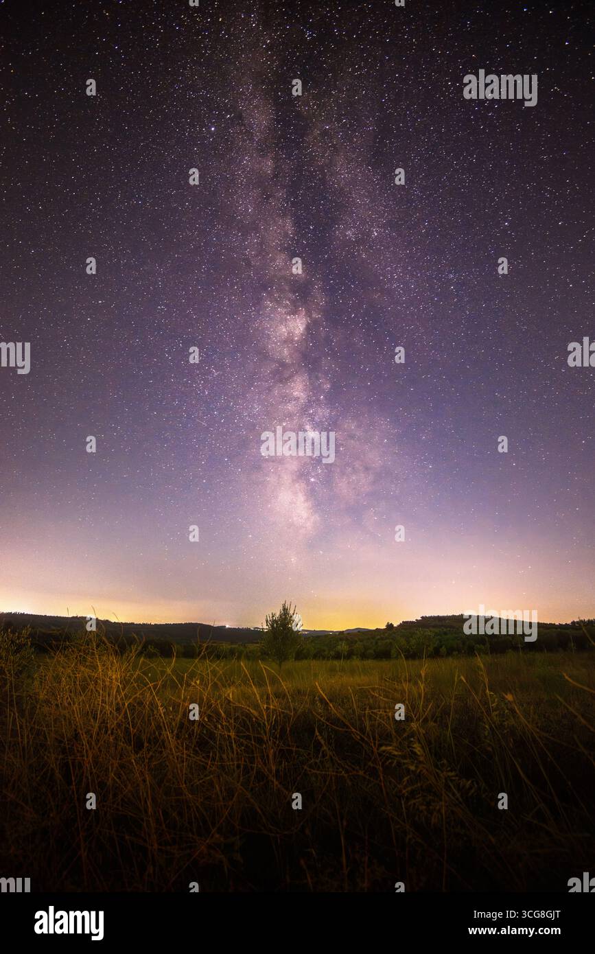 Vista dell'etereo bagliore della via Lattea che dipinge il cielo notturno sopra campi dorati e colline lontane, un paesaggio sereno, Belsh, Qarku i Elbasanit, Albania. Foto Stock
