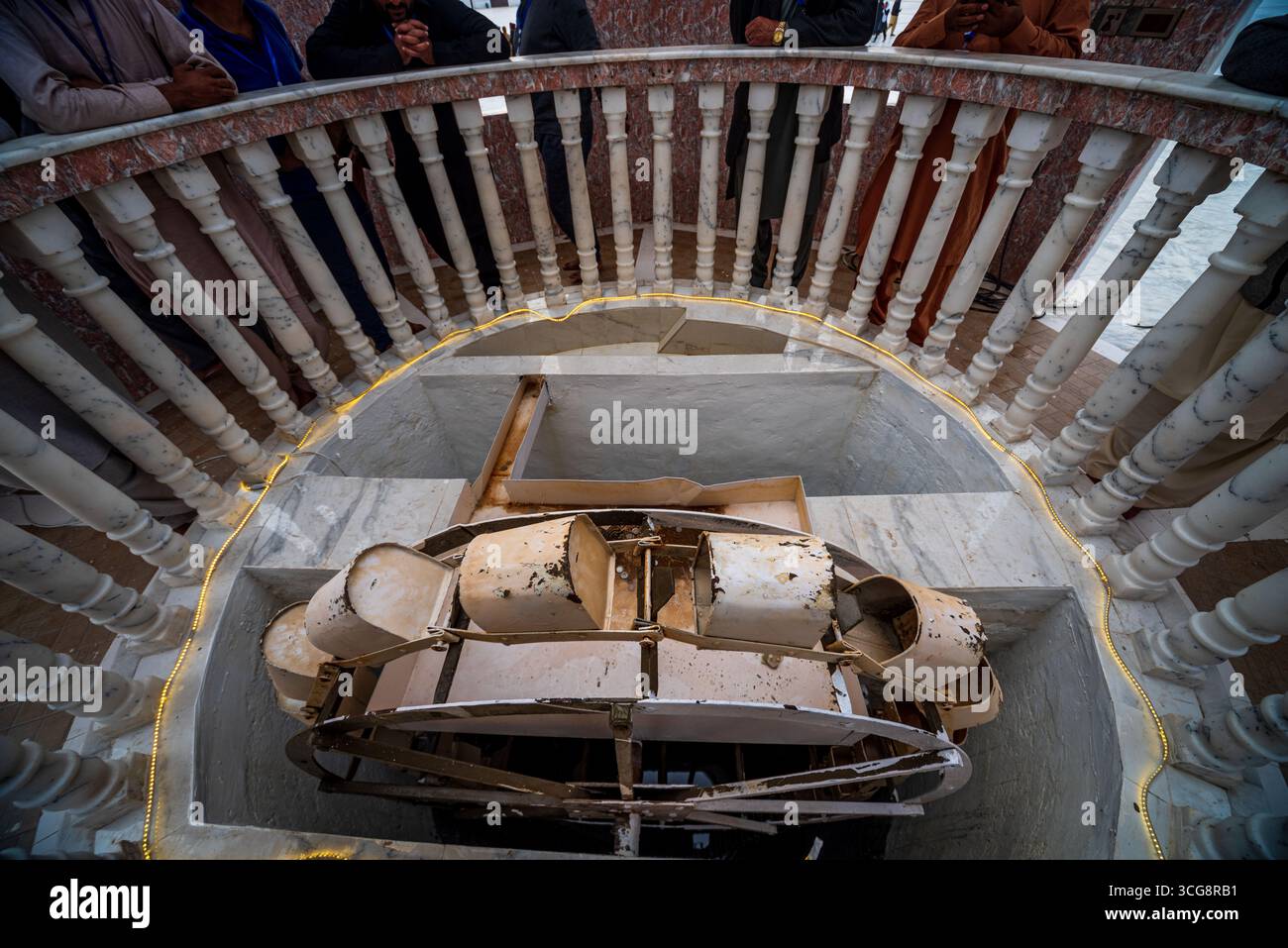 Veduta di un vecchio meccanismo arrugginito con ruota a secchio all'interno di una struttura in pietra, osservata da una ringhiera in marmo ornato sopra, Kartarpur, Punjab, Pakistan. Foto Stock