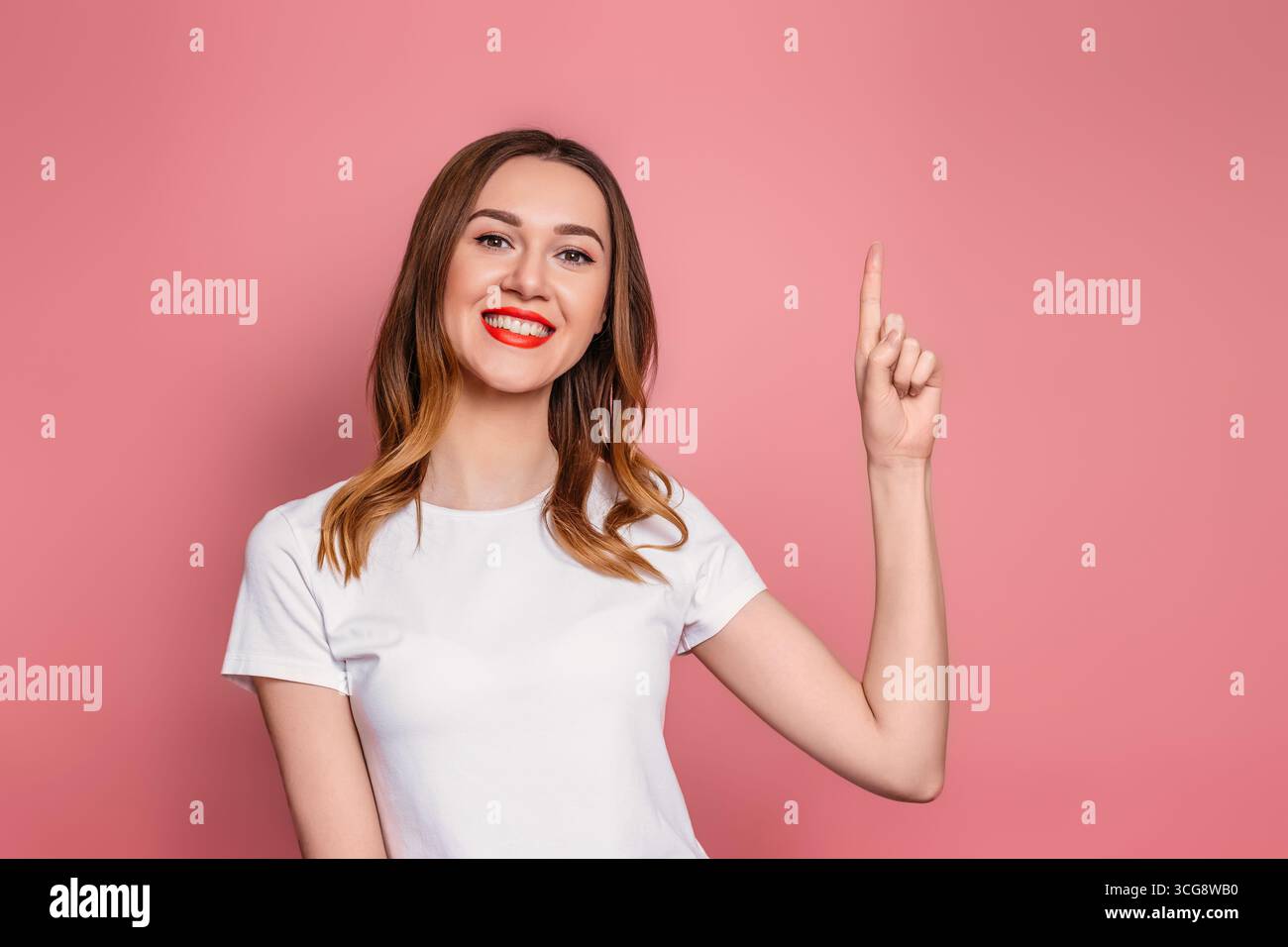 Donna caucasica in t-shirt bianca con labbra rosse sorridenti e con pollice su isolato su sfondo rosa Foto Stock