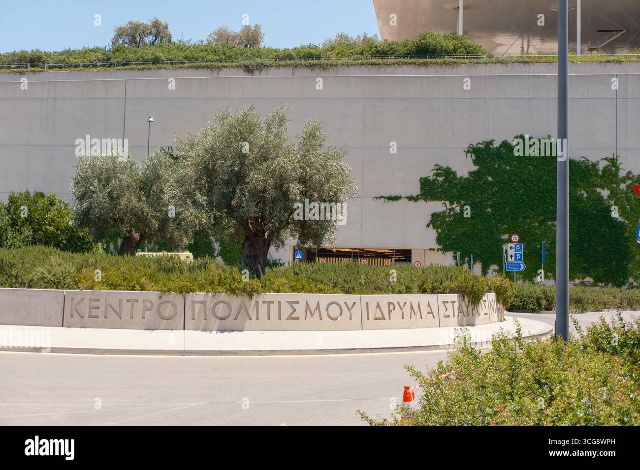 La vista degli ulivi si erge orgogliosamente contro le austere pareti di cemento e la vegetazione lussureggiante, con texture contrastanti ad Athina, Attica, Grecia. Foto Stock