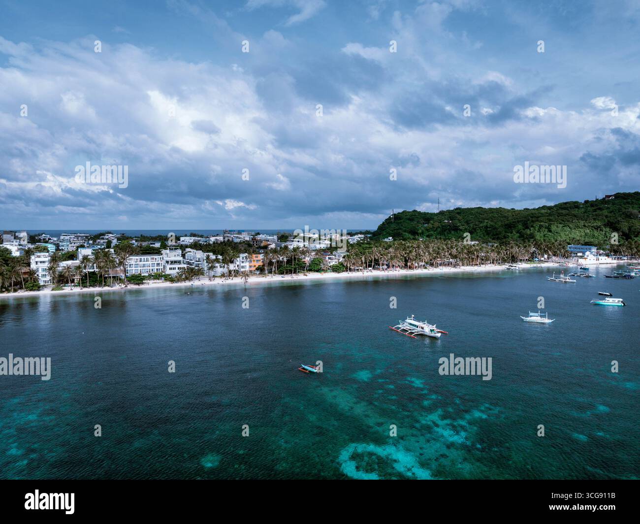 Vista aerea delle acque turchesi incontra le sabbie bianche incontaminate della costa di Boracay, delimitata da colline verdeggianti e punteggiata di barche sotto un cielo spettacolare, malesi, Visayas occidentali, Filippine. Foto Stock