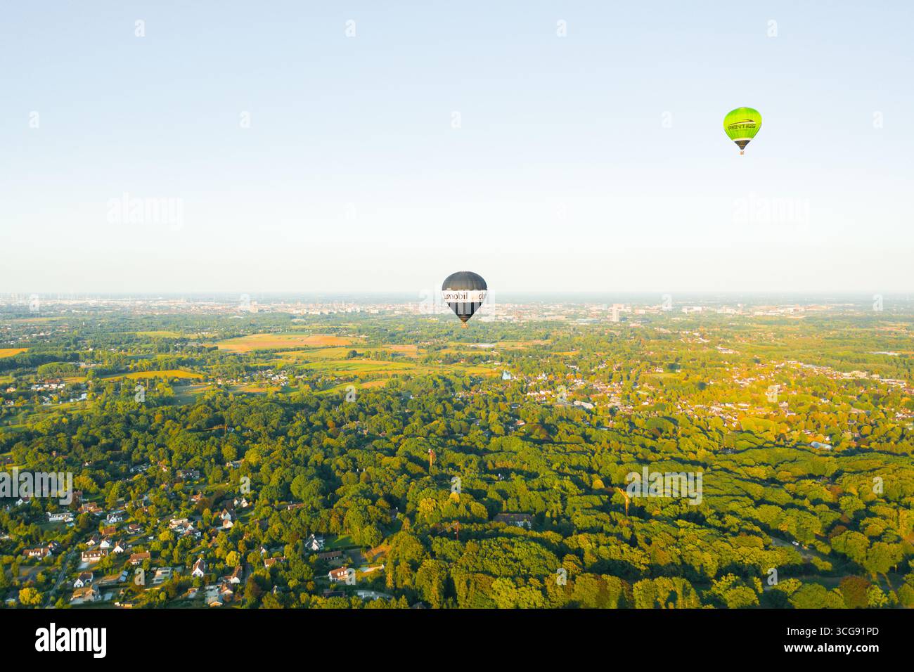 Sint-Martens-Latem, Belgio - 25 agosto 2025: Veduta aerea di due mongolfiere che volano sopra una vivace tettoia verde, la scena è immersa nella morbida Foto Stock