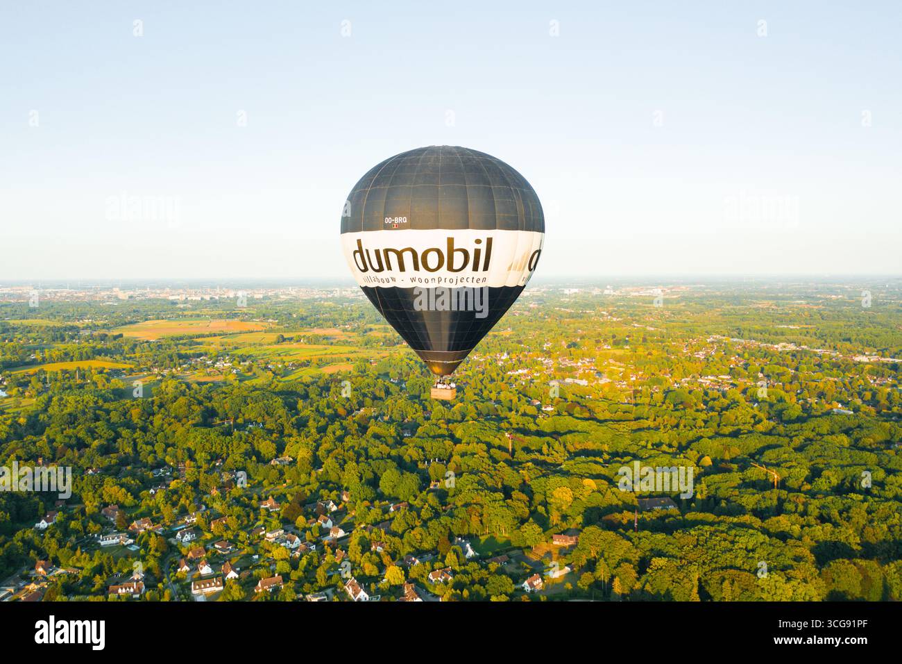 Sint-Martens-Latem, Belgio - 25 agosto 2025: Veduta aerea di una mongolfiera a marchio dumobil che si sposta serenamente su un arazzo verdeggiante di fitta foresta e tetti sparsi. Foto Stock