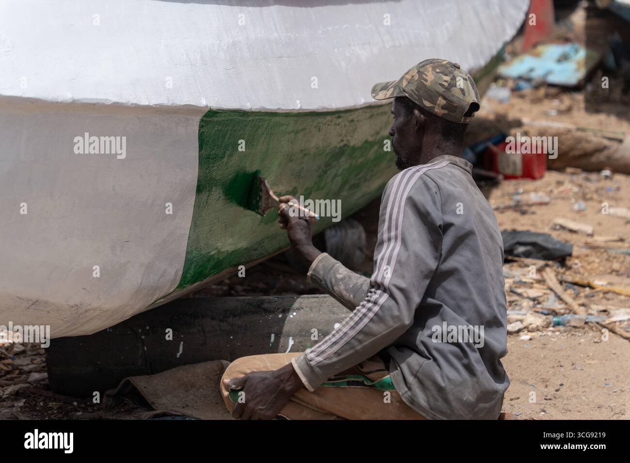 Dakar, Senegal - 12 maggio 2025: Veduta di un uomo dipinge meticolosamente lo scafo di una barca a Soumbédioune, colori che si mescolano sotto il sole duro. Foto Stock