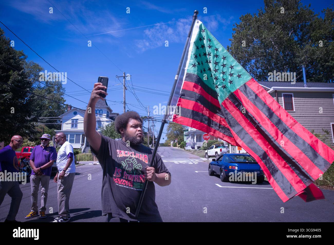 Alla African American Day Parade. Un giovane si fa un selfie con la bandiera verde nera rossa afro americana. A Nyack, Rockland County, New York. Foto Stock