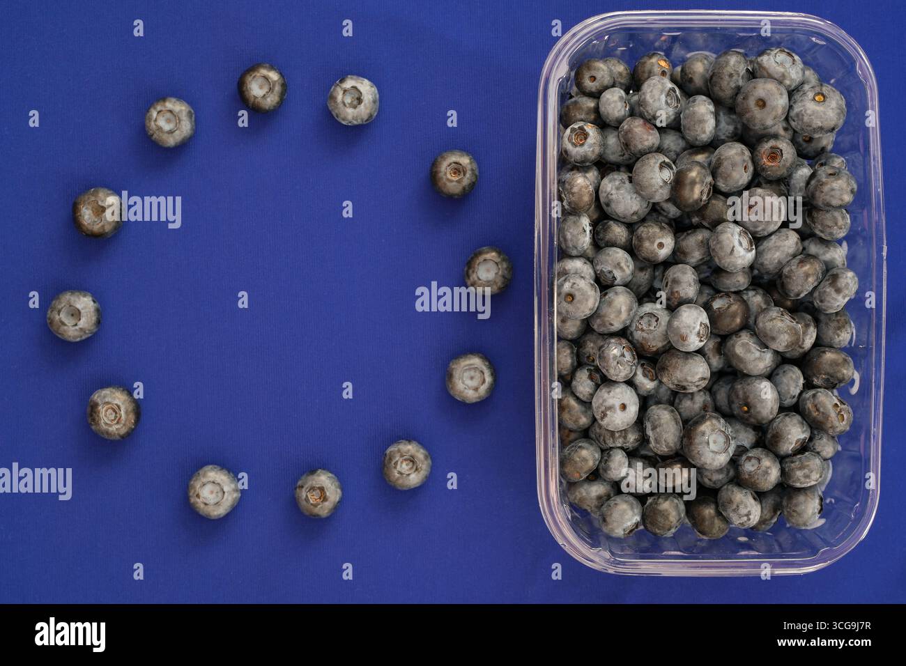 Contenitore in plastica con mirtilli. I mirtilli imitano le stelle della bandiera dell'UE. Produzione e commercio di bacche nell'Unione europea. Copia spazio. Foto Stock