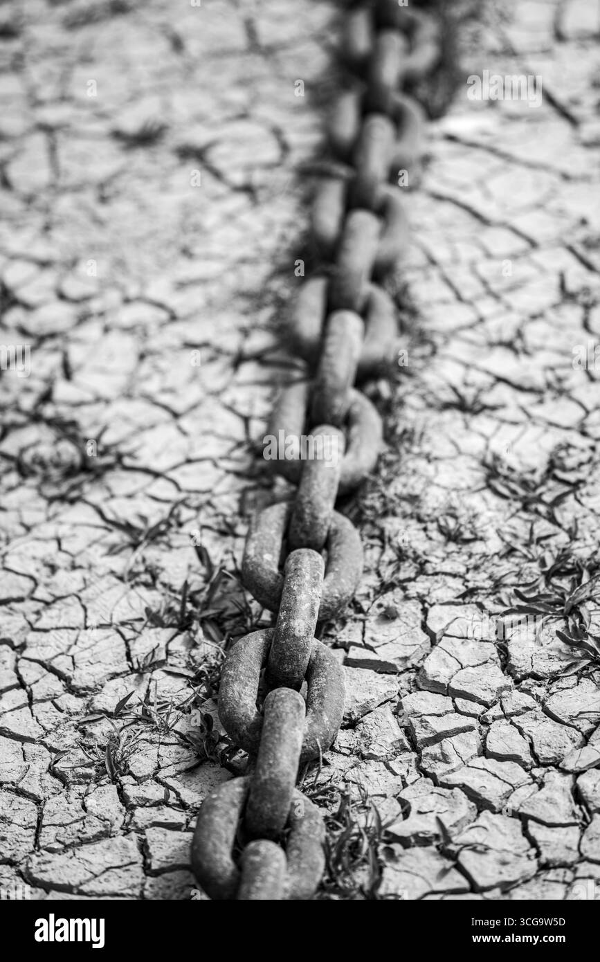 Foto in bianco e nero di una catena arrugginita su un terreno asciutto incrinato. Foto Stock
