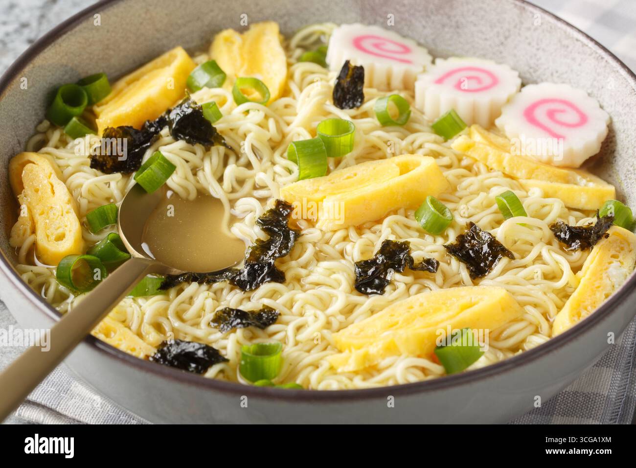 Zuppa di noodle hawaiana Saimin con nori, omelette, kamaboko e cipolle verdi in primo piano nel piatto sul tavolo. Orizzontale Foto Stock