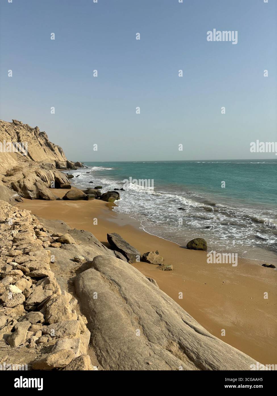 Spiaggia di sabbia dorata con onde turchesi e scogliere di arenaria lungo la costa del Golfo Persico nel sud dell'Iran. Foto Stock