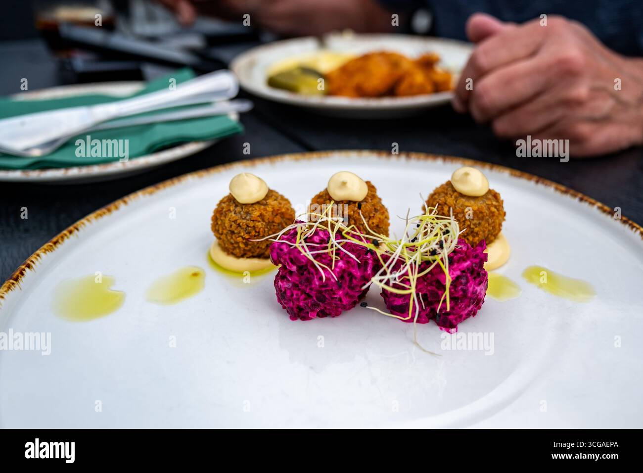Antipasto a base di barbabietole e palla d'anatra su piatto bianco in primo piano. Schnitzel con purè di patate e mano, posate e asciugamano sullo sfondo. In RIS Foto Stock