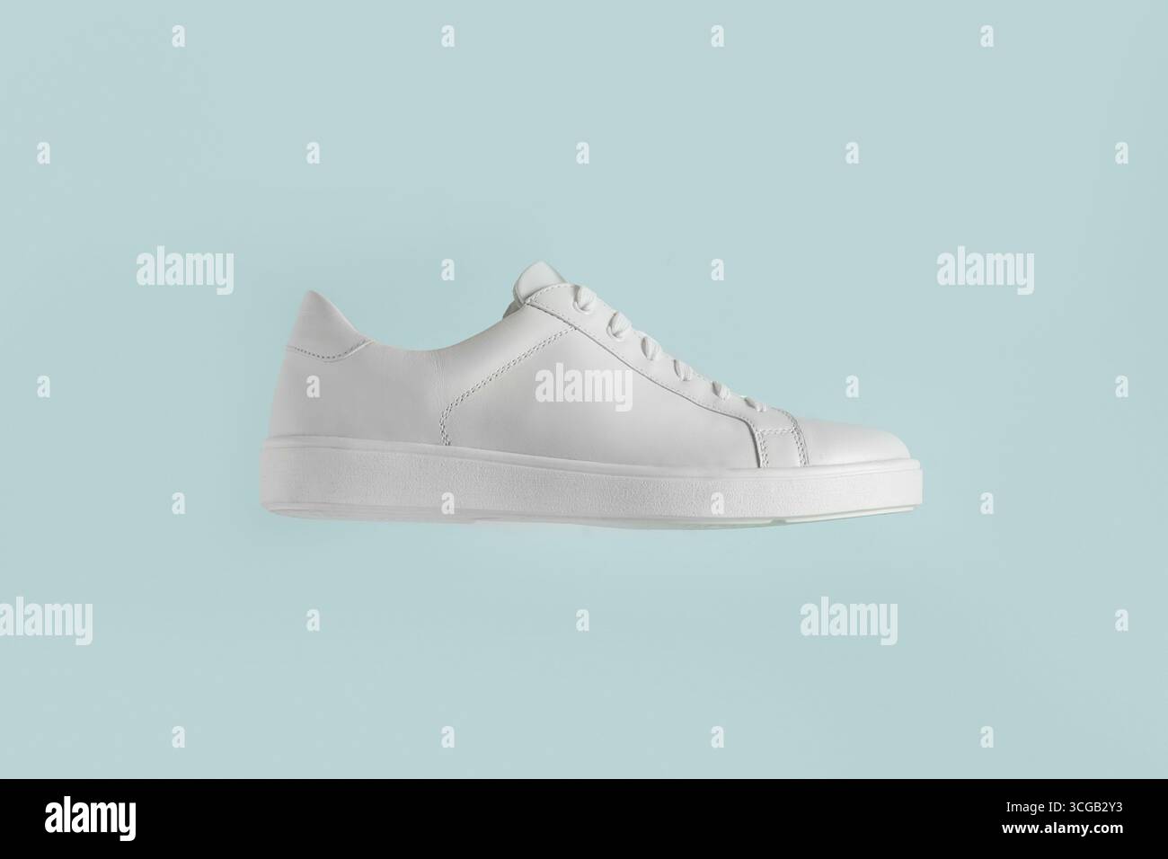 Donna che tiene a mano una nuova sneaker bianca elegante e pulita su sfondo azzurro. Lo stile moderno, la moda e il concetto di calzature della scarpa. Copia spazio. Foto Stock