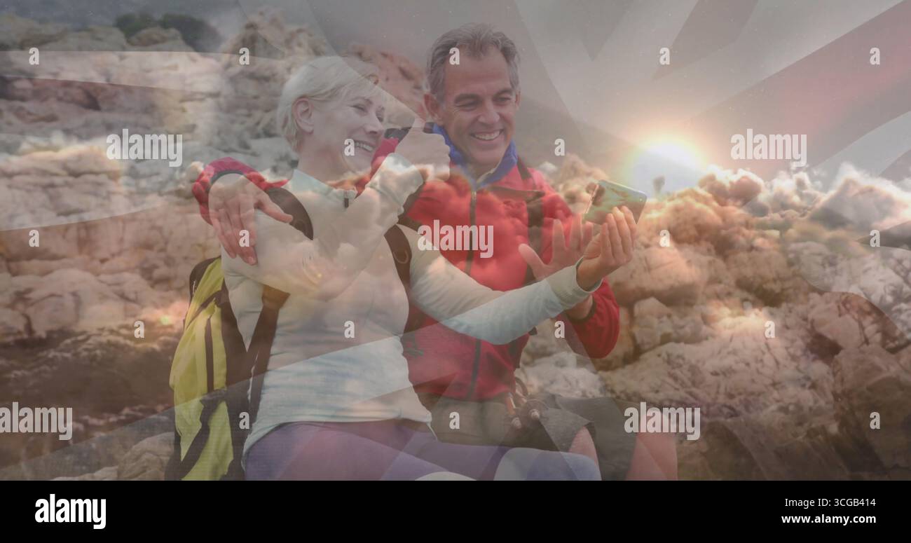 Coppia senior sorridente che scatta selfie sulle rocce costiere in acqua, con zaini da trekking e smartphone Foto Stock